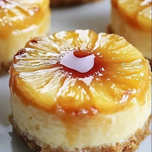 Mini pineapple upside-down cheesecakes topped with cherries on white plate.