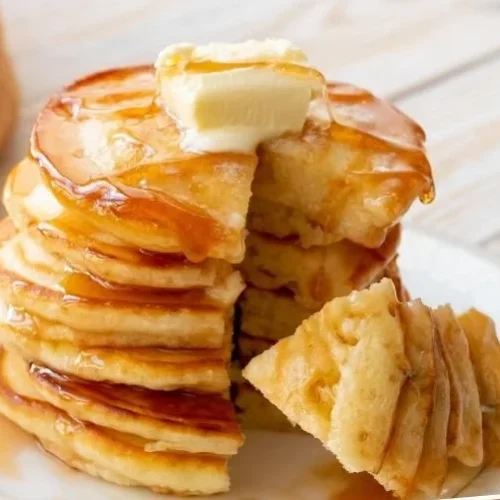 Fluffy buttermilk pancakes stacked on a plate, drizzled with syrup and fresh berries.