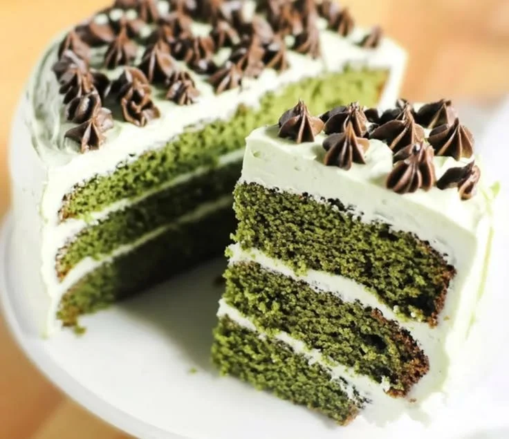 A slice of Green Velvet Cake topped with cream cheese frosting and decorative sprinkles.