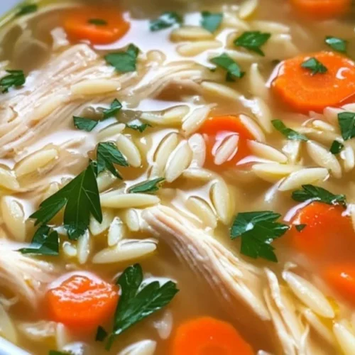 Bowl of lemon chicken orzo soup garnished with fresh herbs and lemon slices.