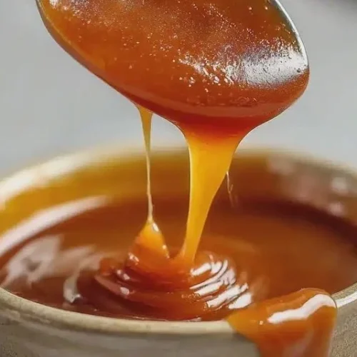 Delicious homemade caramel sauce in a glass jar with a drizzle on top.